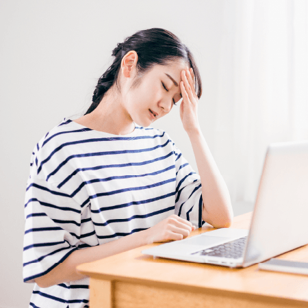 頭痛を我慢しながらパソコン作業をする女性