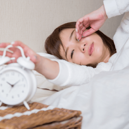 寝ぼけ眼で目覚まし時計を止める女性